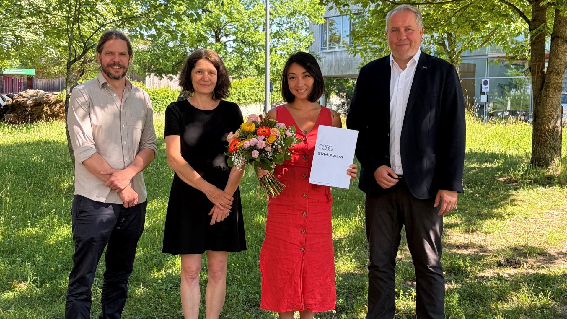 Vier Personen posieren mit dem SMR Award und einem Blumenstrauß.